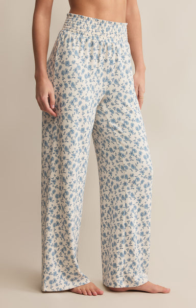 A pair of high-waisted, full-length pants with a smocked waistband and a blue floral pattern on a white background.