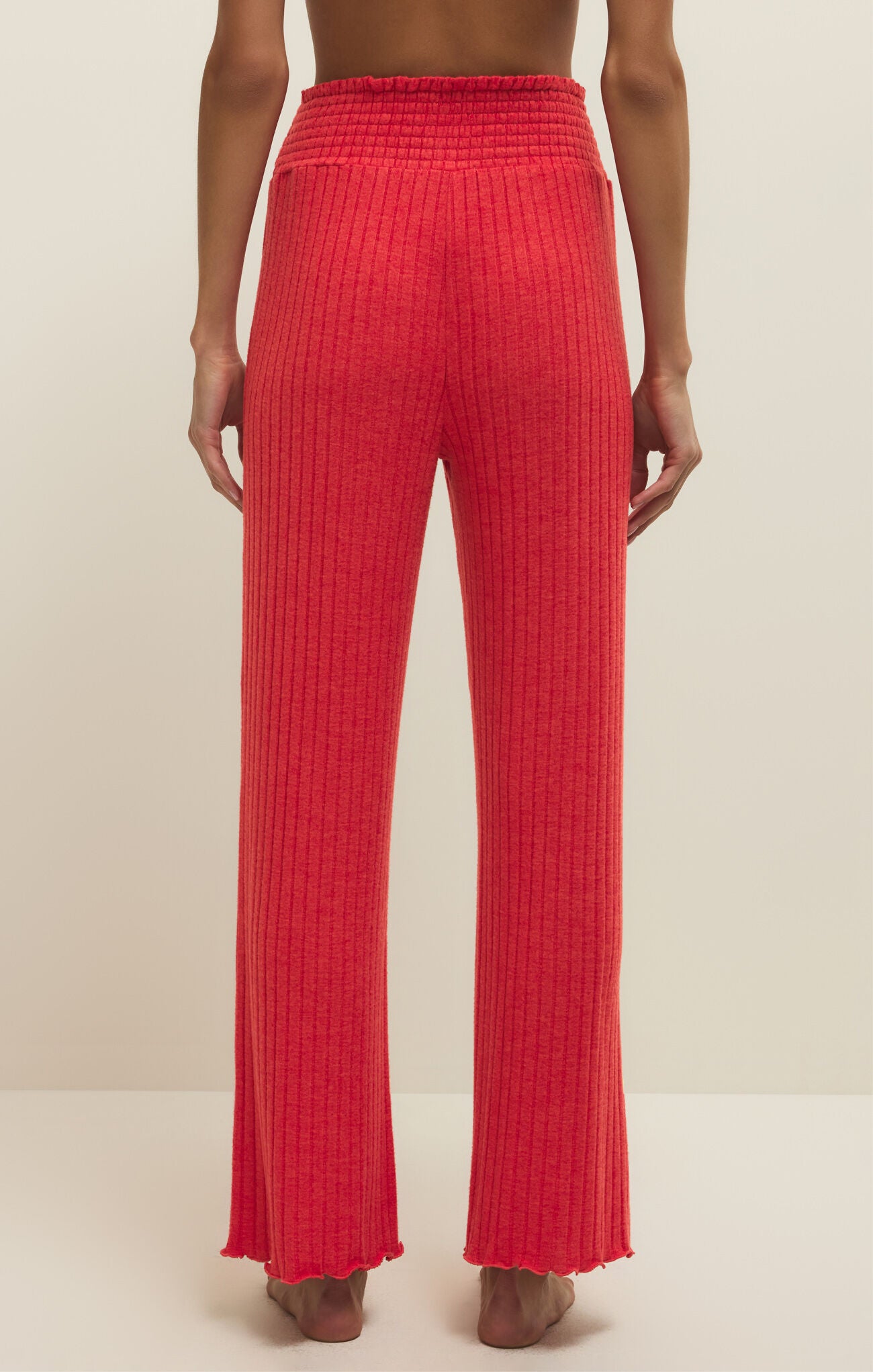 Red ribbed pants worn by a person on a beige background