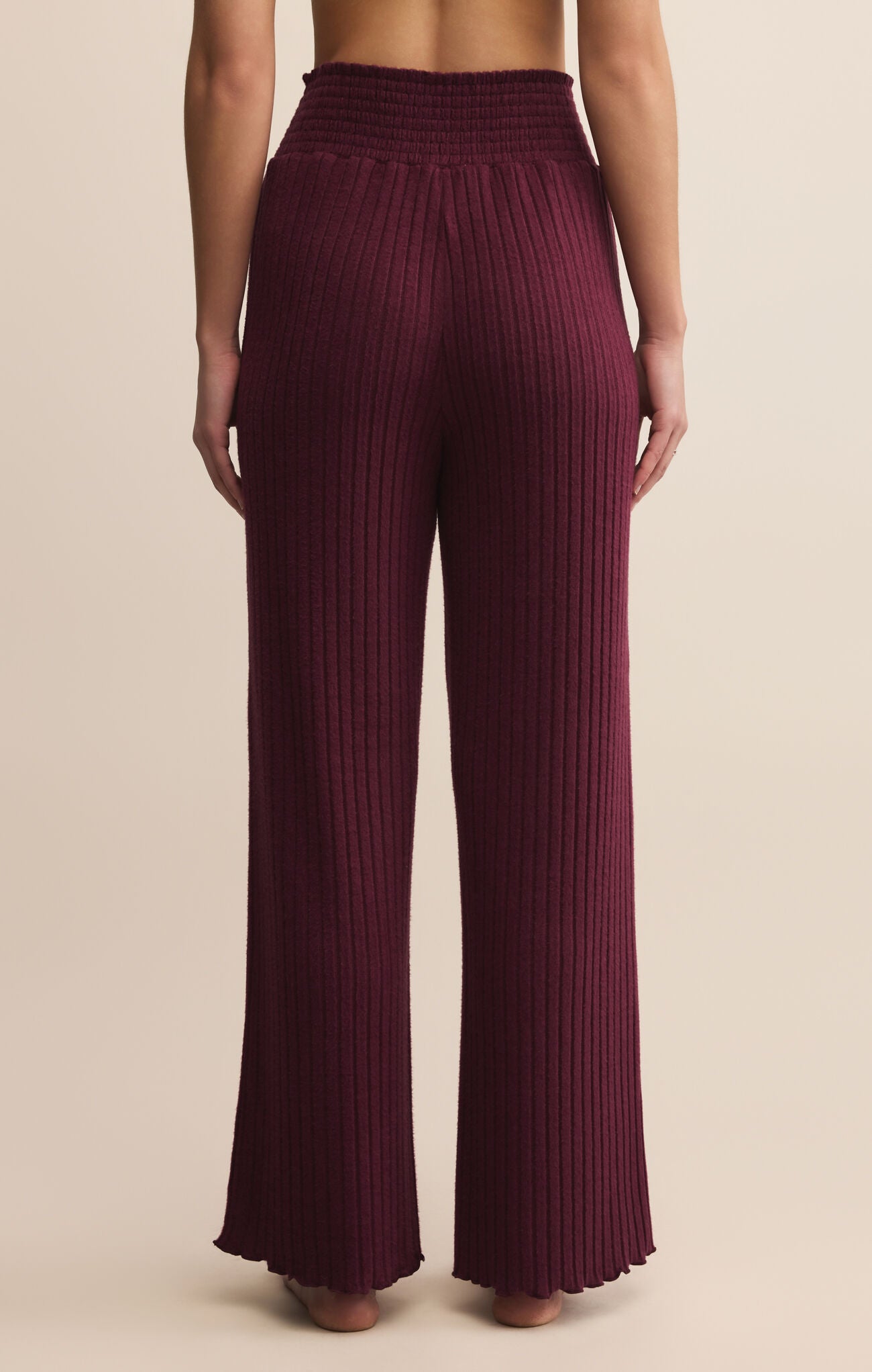 Maroon ribbed pants worn by a person on a beige background