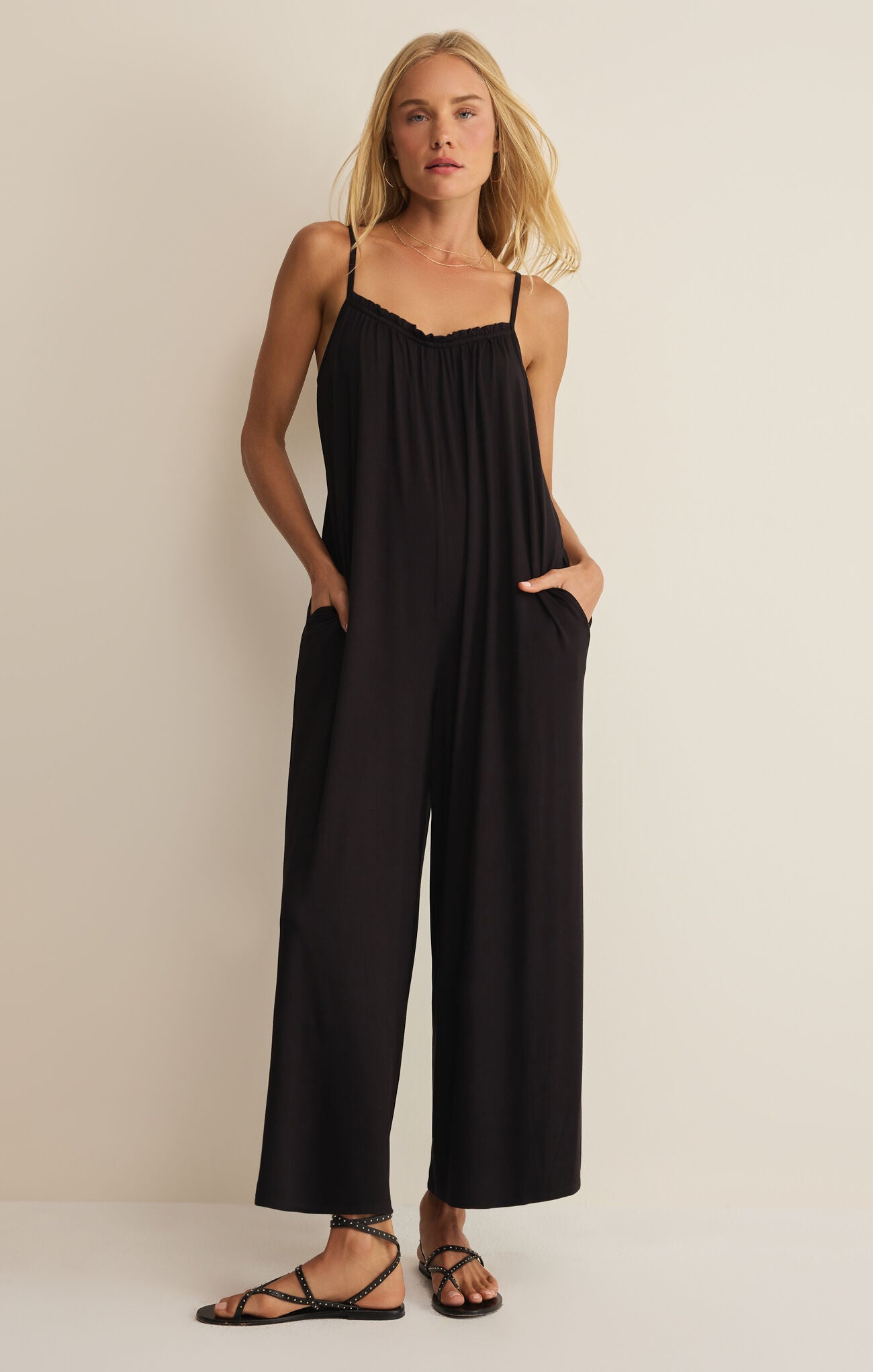 Woman wearing a black jumpsuit against a beige background