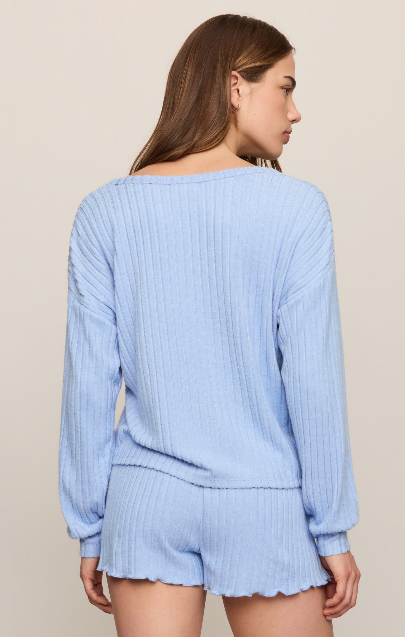 Woman wearing a light blue ribbed sweater and shorts set against a beige background