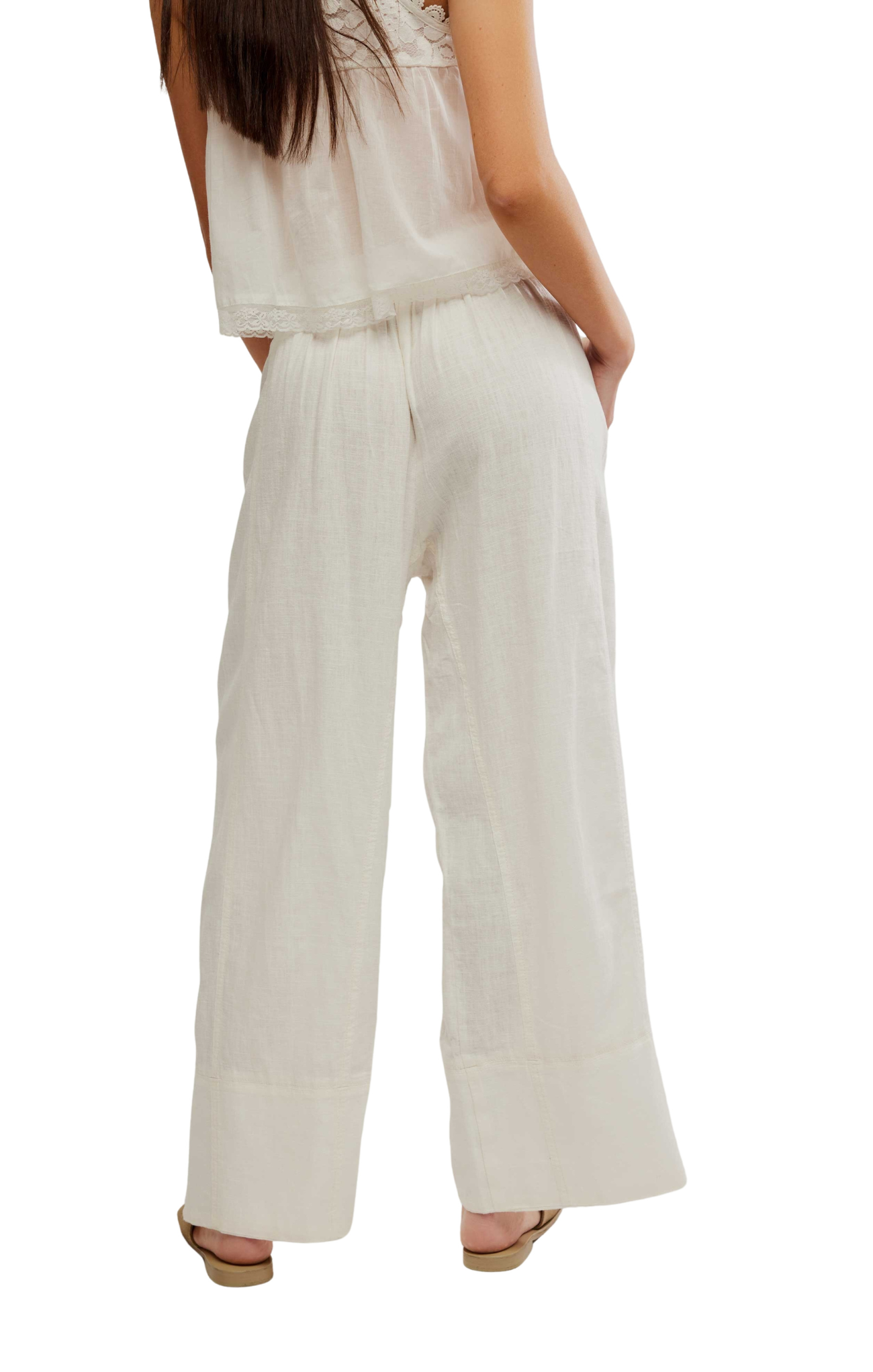 Person wearing a light-colored sleeveless top and wide-leg pants on a white background