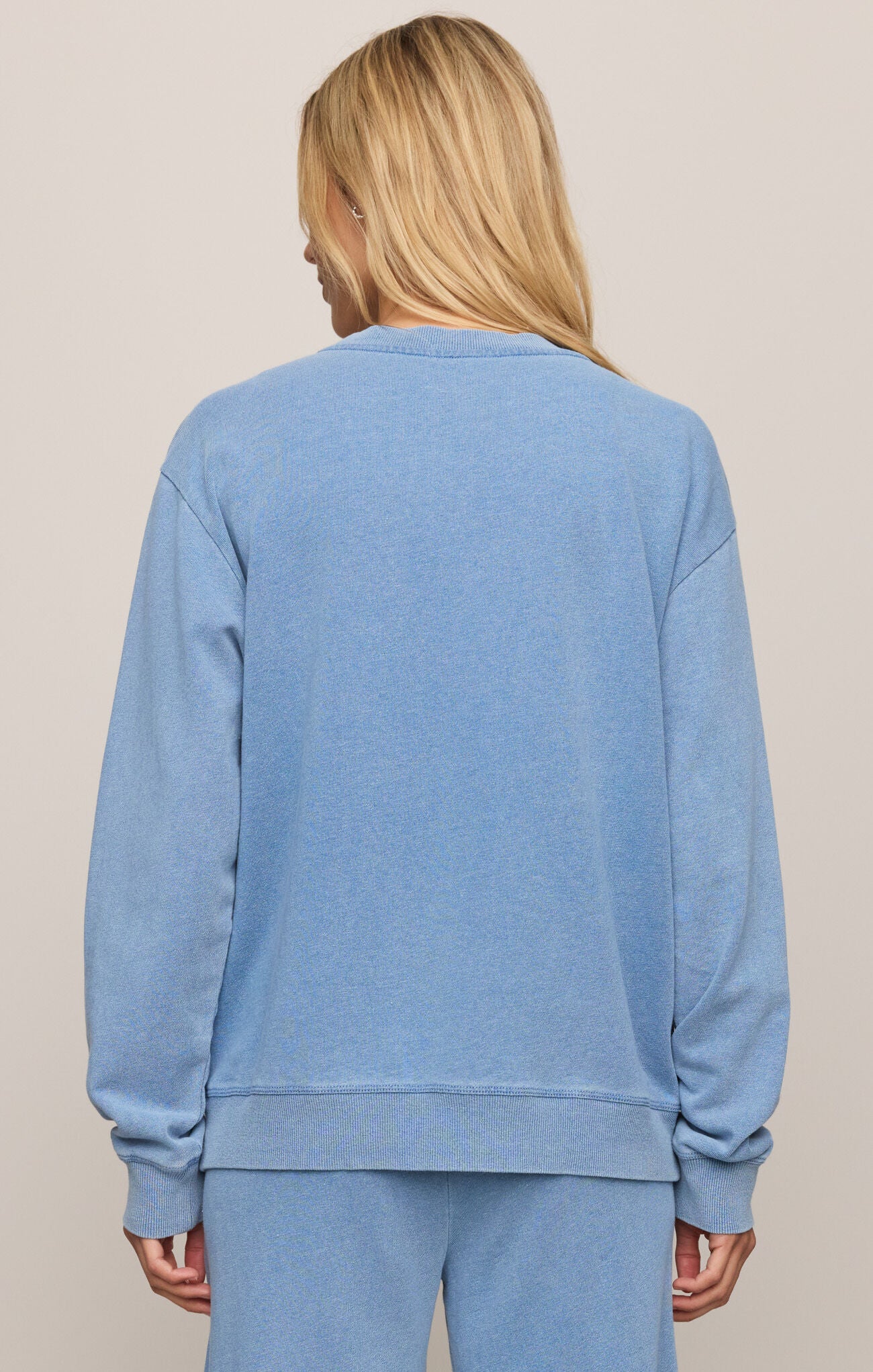 Person wearing a blue sweatshirt and pants set against a beige background