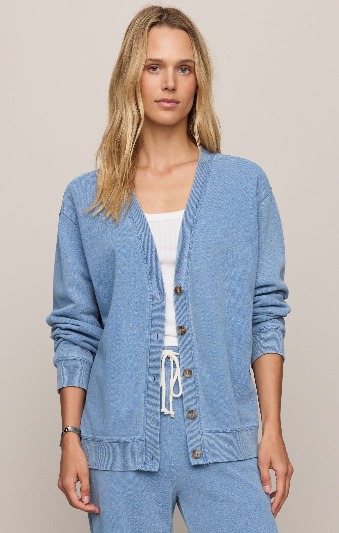 Woman wearing a blue cardigan over a white top and blue pants on a beige background