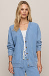 Woman wearing a blue cardigan over a white top and blue pants on a beige background