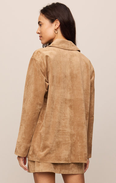 Woman wearing a brown suede jacket against a beige background
