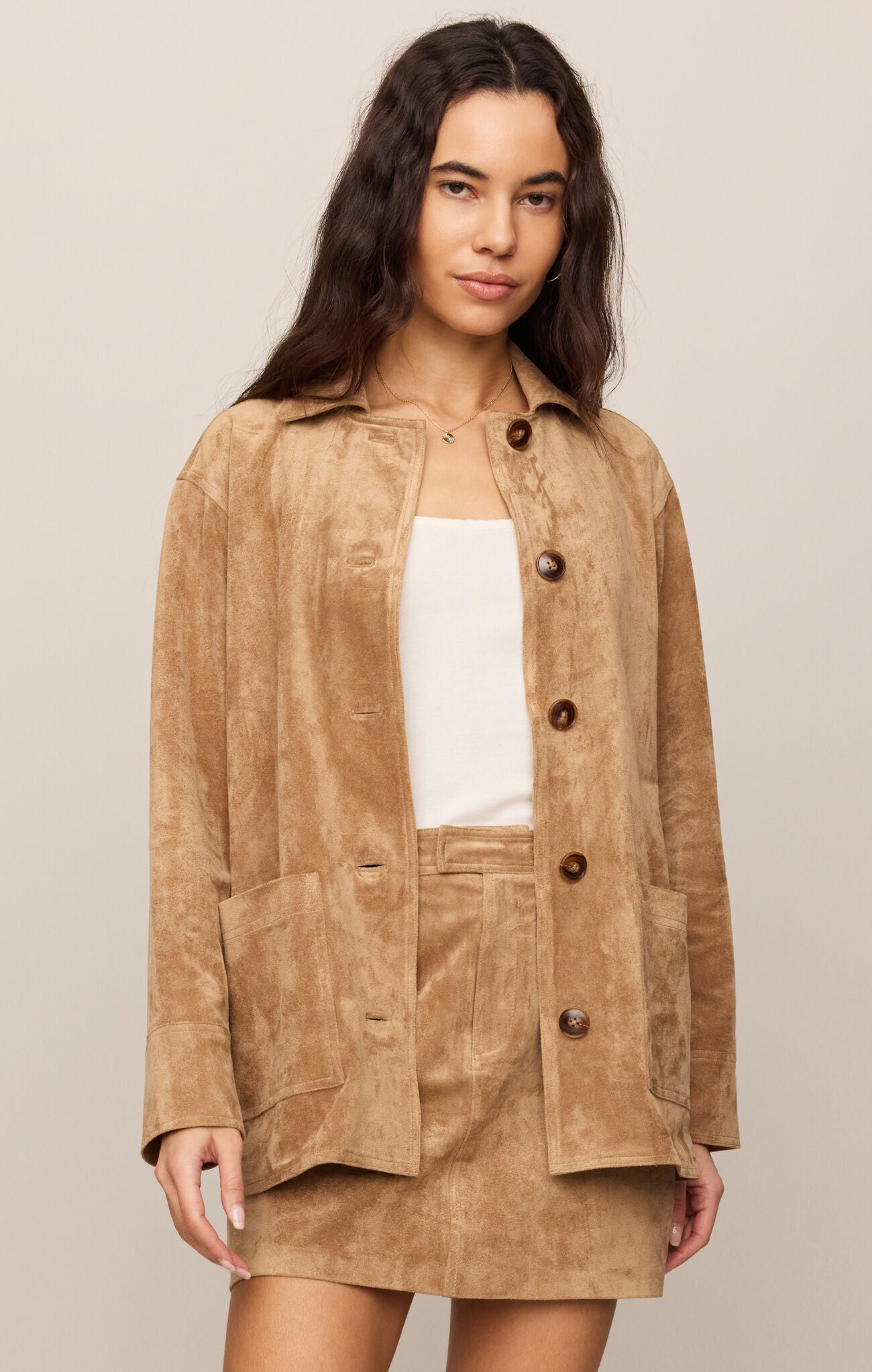 Woman wearing a brown suede jacket and skirt set on a beige background
