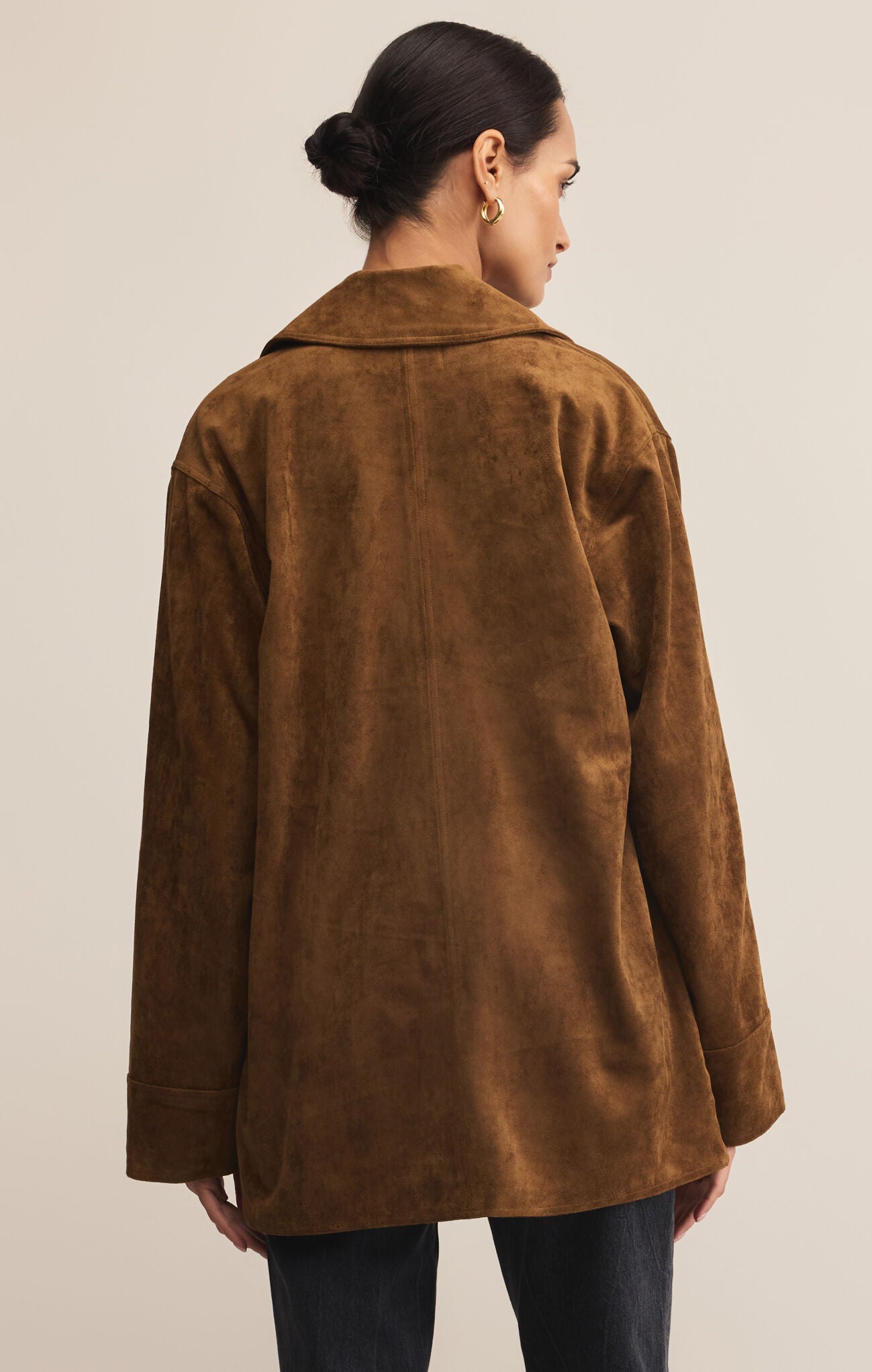 Person wearing a brown suede jacket on a plain background