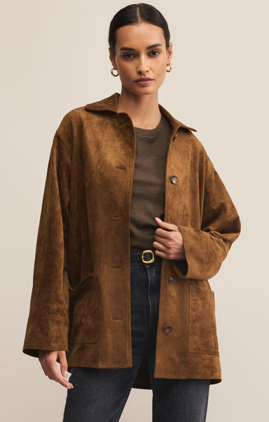 A female model wearing a brown collared long sleeve button front suede chore jacket with patch pockets.