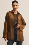 A female model wearing a brown collared long sleeve button front suede chore jacket with patch pockets.