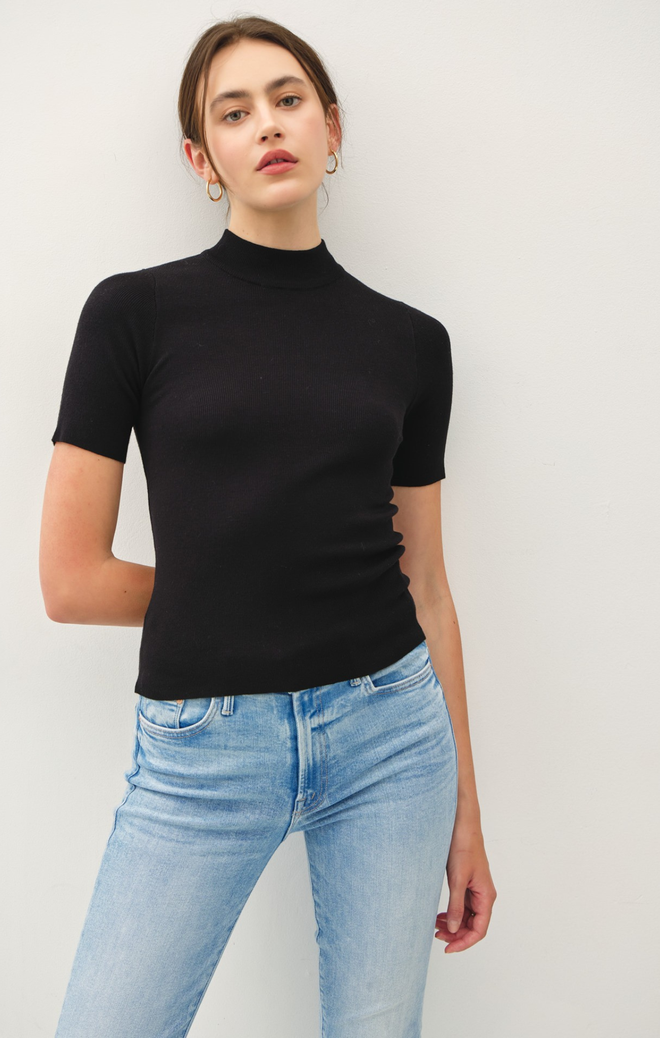 Person wearing a black turtleneck and light blue jeans against a white background