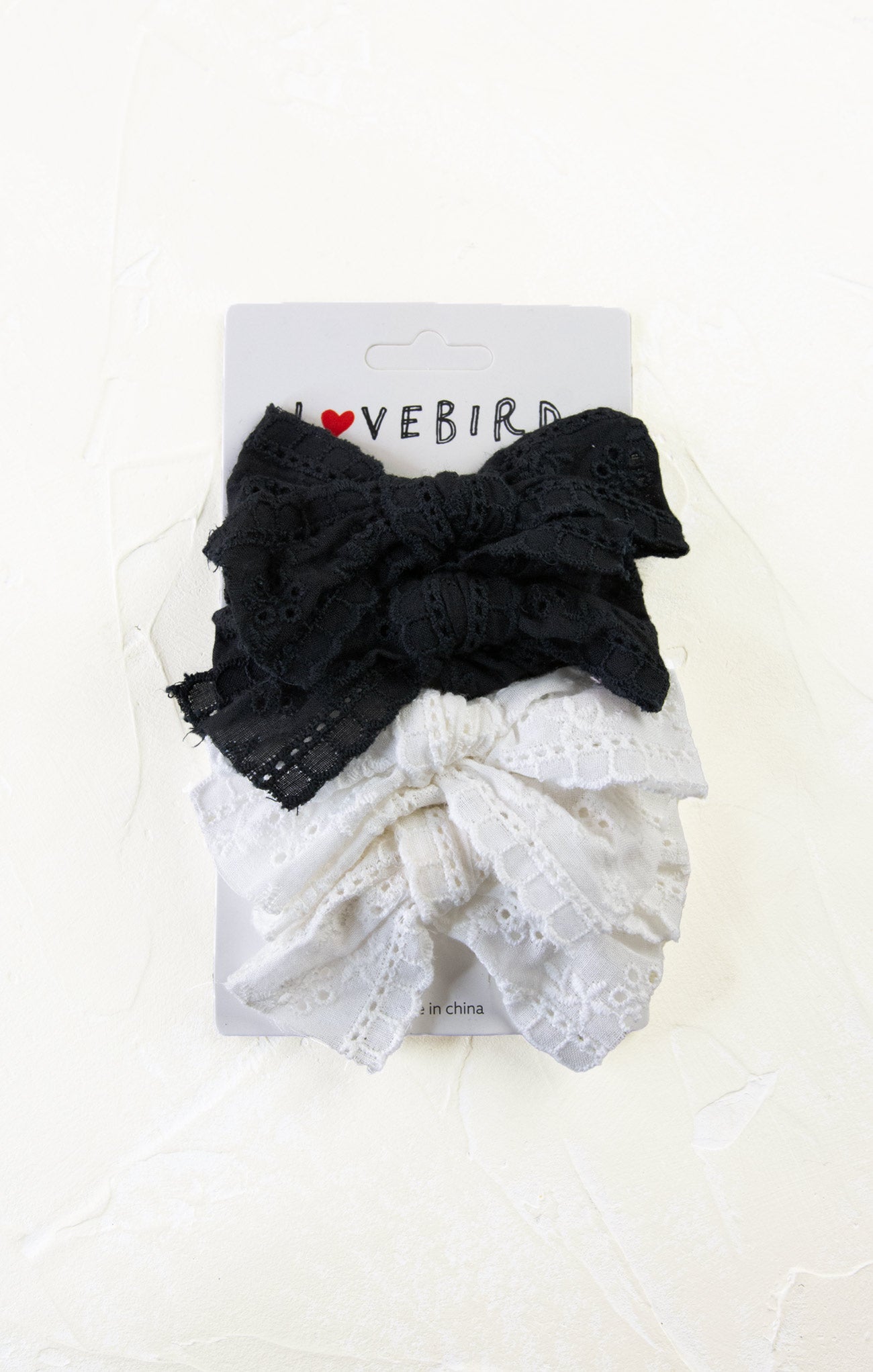 Two hair bows, one black and one white with lace details, on a Lovebird branded card.