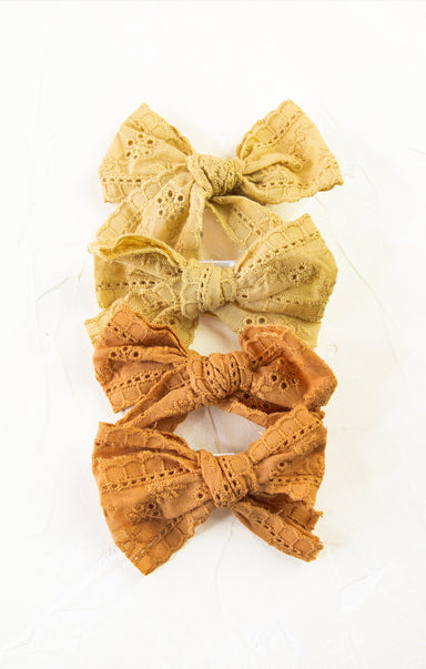 Three lace bows in yellow, green, and orange on a white background