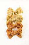 Three lace bows in yellow, green, and orange on a white background