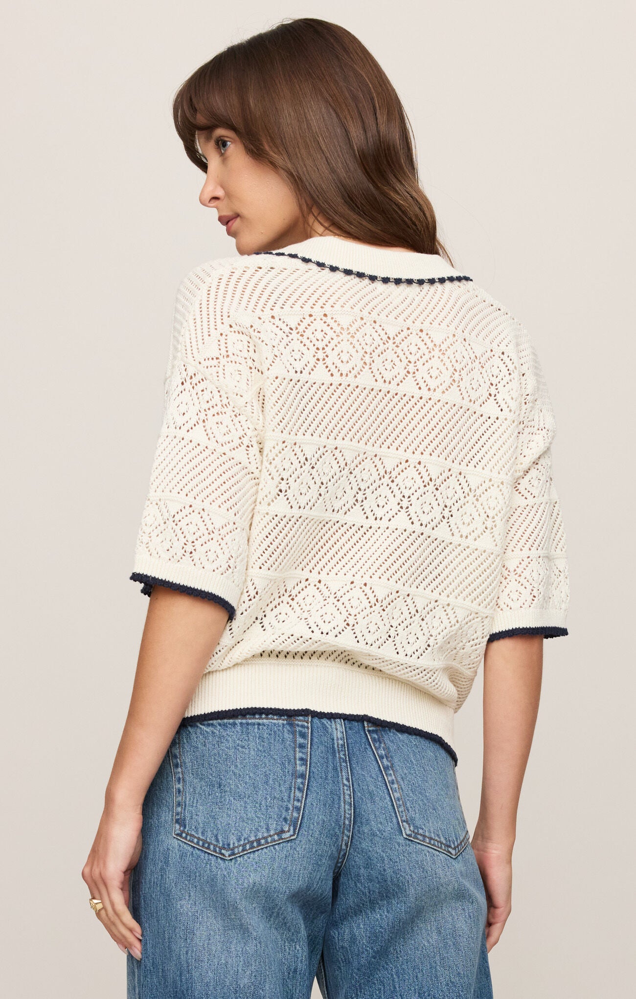 Woman wearing a white lace top with blue jeans on a plain background