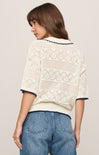 Woman wearing a white lace top with blue jeans on a plain background