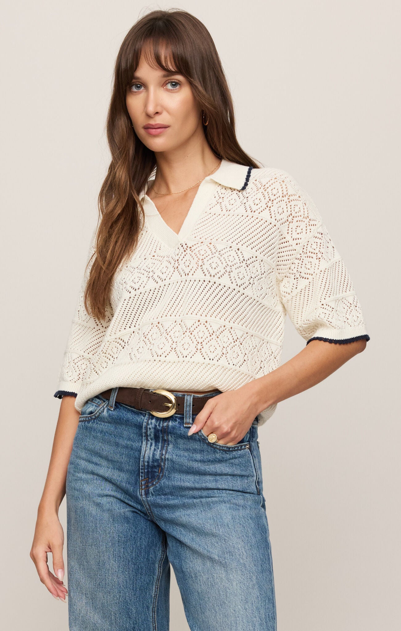 Woman wearing a white lace top and blue jeans against a plain background