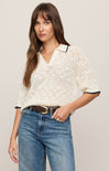 Woman wearing a white lace top and blue jeans against a plain background