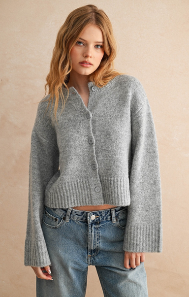 Woman wearing a gray cardigan and blue jeans against a beige background