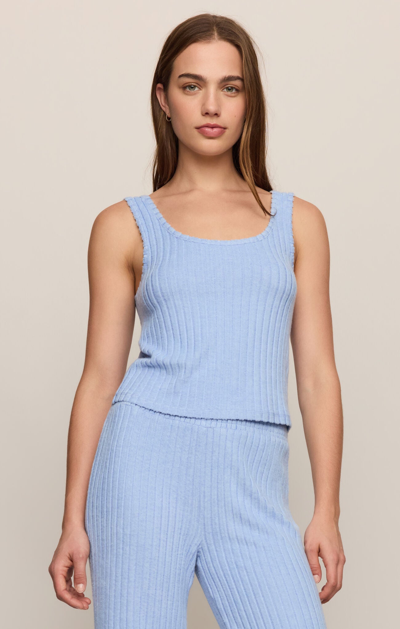 Woman wearing a light blue ribbed sleeveless top and pants against a beige background