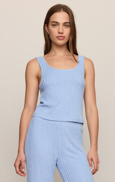 Woman wearing a light blue ribbed sleeveless top and pants against a beige background