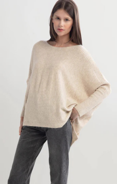 Woman wearing a beige sweater and dark pants on a white background