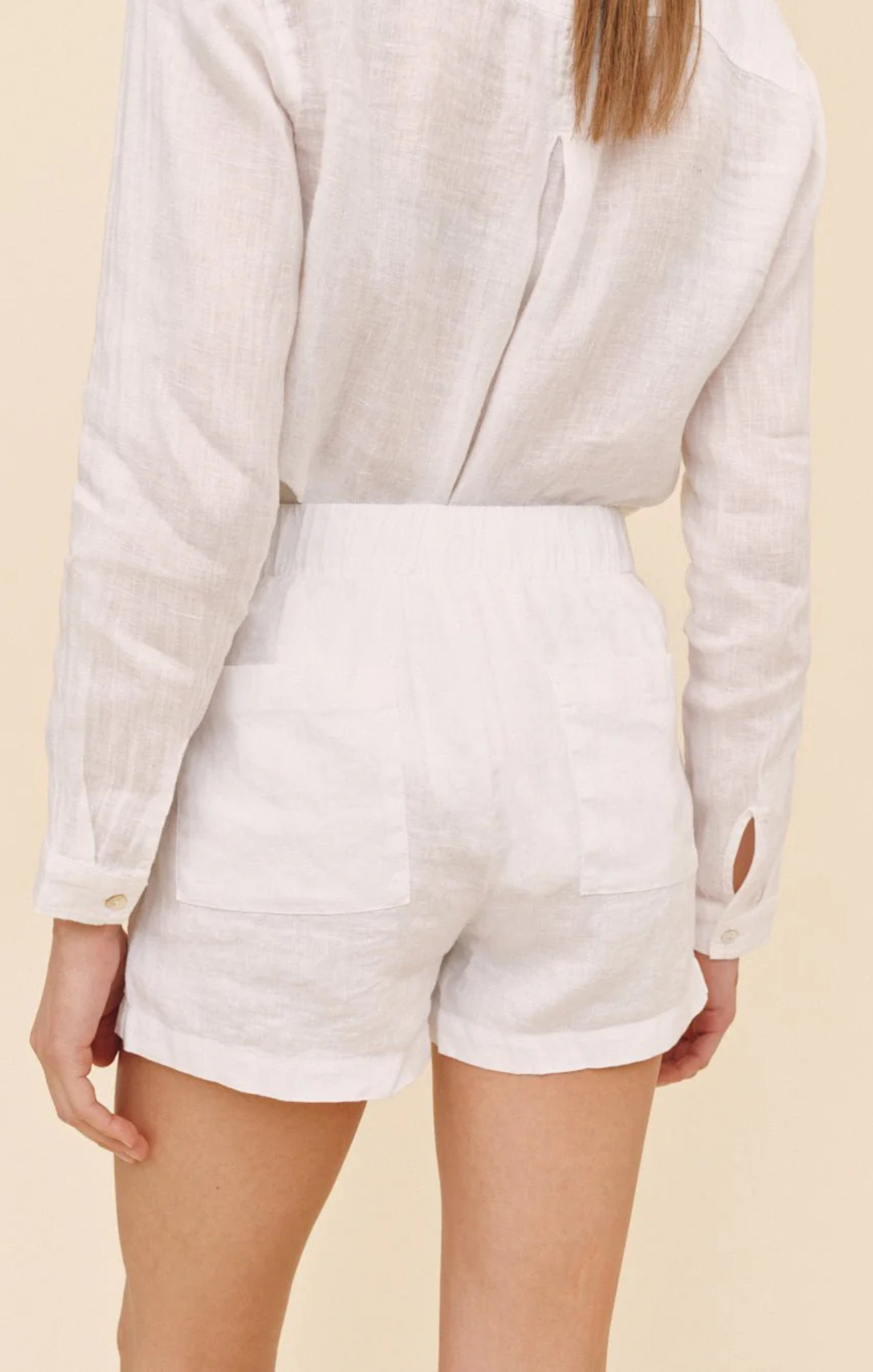 Person wearing a light-colored long-sleeve top and white shorts on a beige background