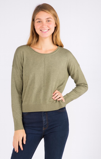 A woman modeling a long-sleeve crewneck knit sweater in sage green, paired with dark blue jeans, against a plain white studio background.