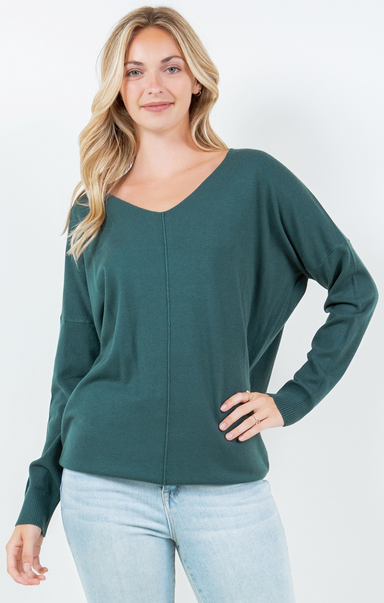 Woman wearing a green sweater and light blue jeans against a white background