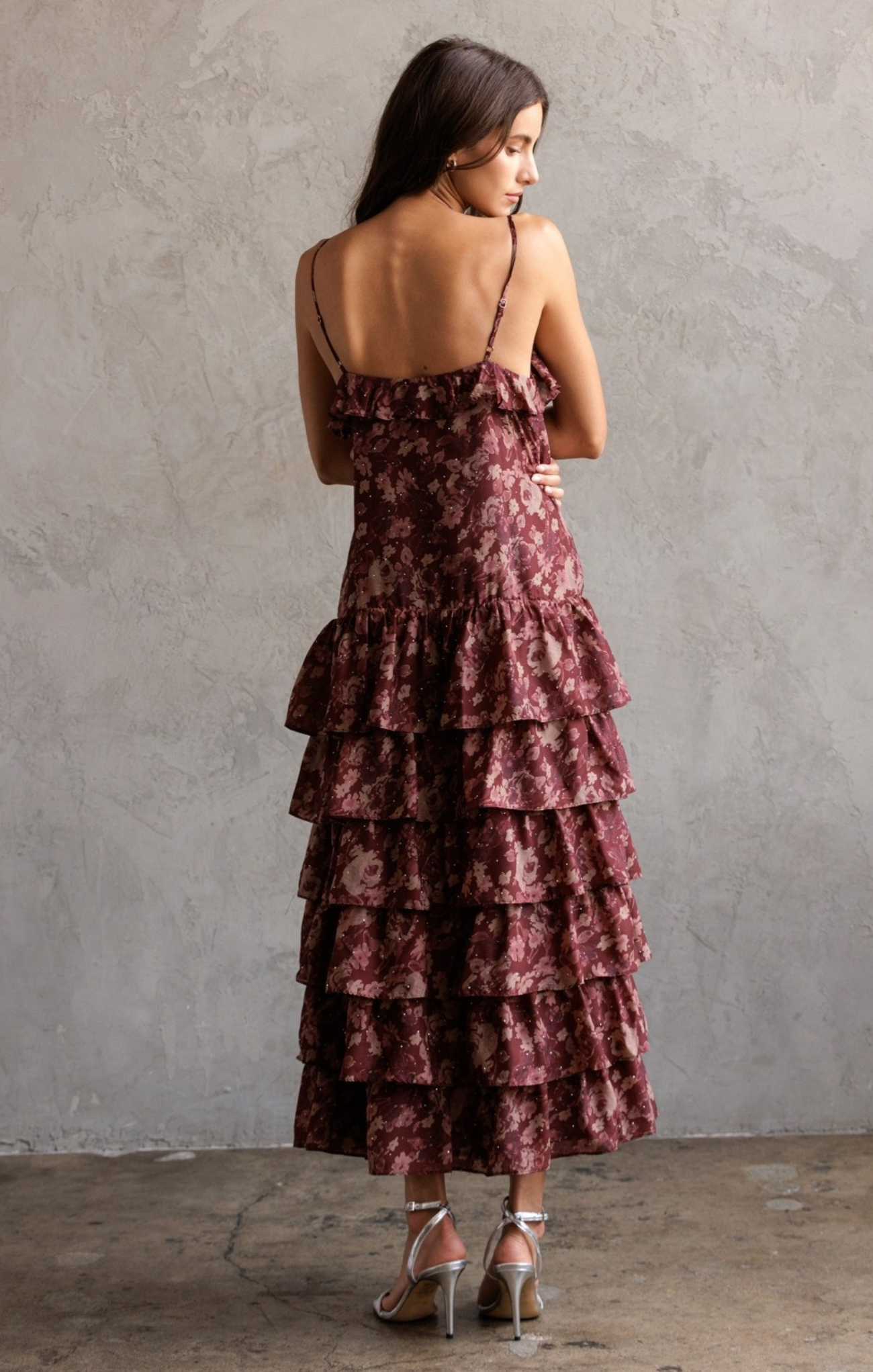 Woman wearing a tiered, floral-patterned dress against a plain wall.