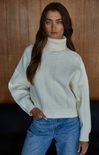 Woman wearing a light blue sweater and blue jeans against a wooden background