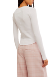 A model shown from the back wearing a fitted white long-sleeve knit top with a scalloped hem and light pink plaid trousers against a plain white background.