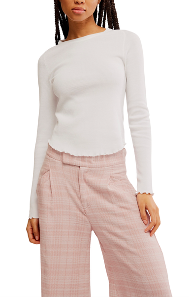 A model wearing a white long-sleeve ribbed knit top with a scalloped hem and light pink plaid trousers, shown from the neck down against a plain white background.