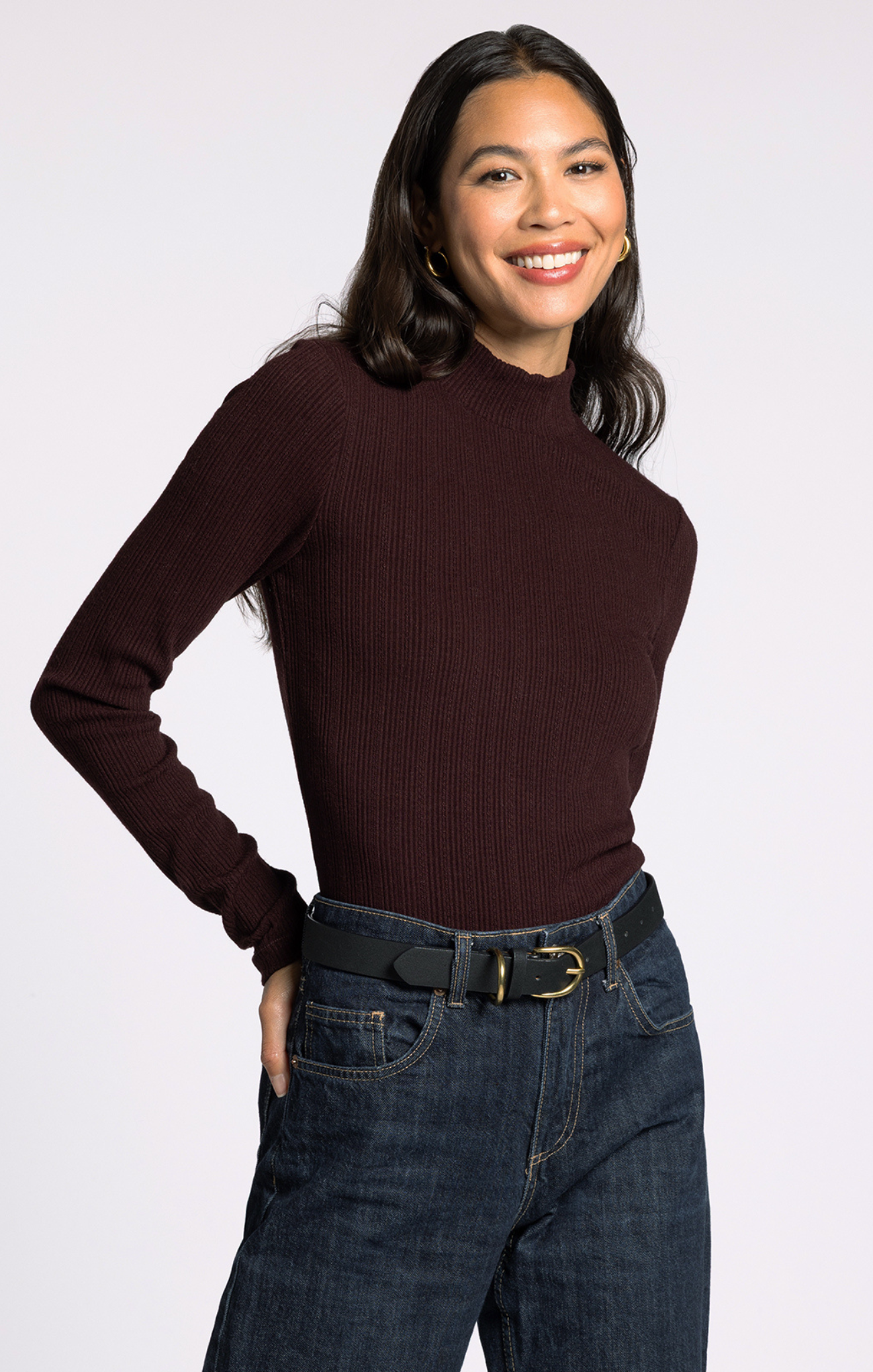 Woman wearing a brown ribbed sweater and blue jeans on a white background