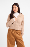 Woman wearing a beige cable knit sweater and brown pants on a white background