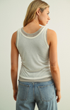 Woman wearing a light gray tank top and blue jeans on a plain background
