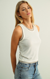 Woman wearing a white tank top and blue jeans against a plain background