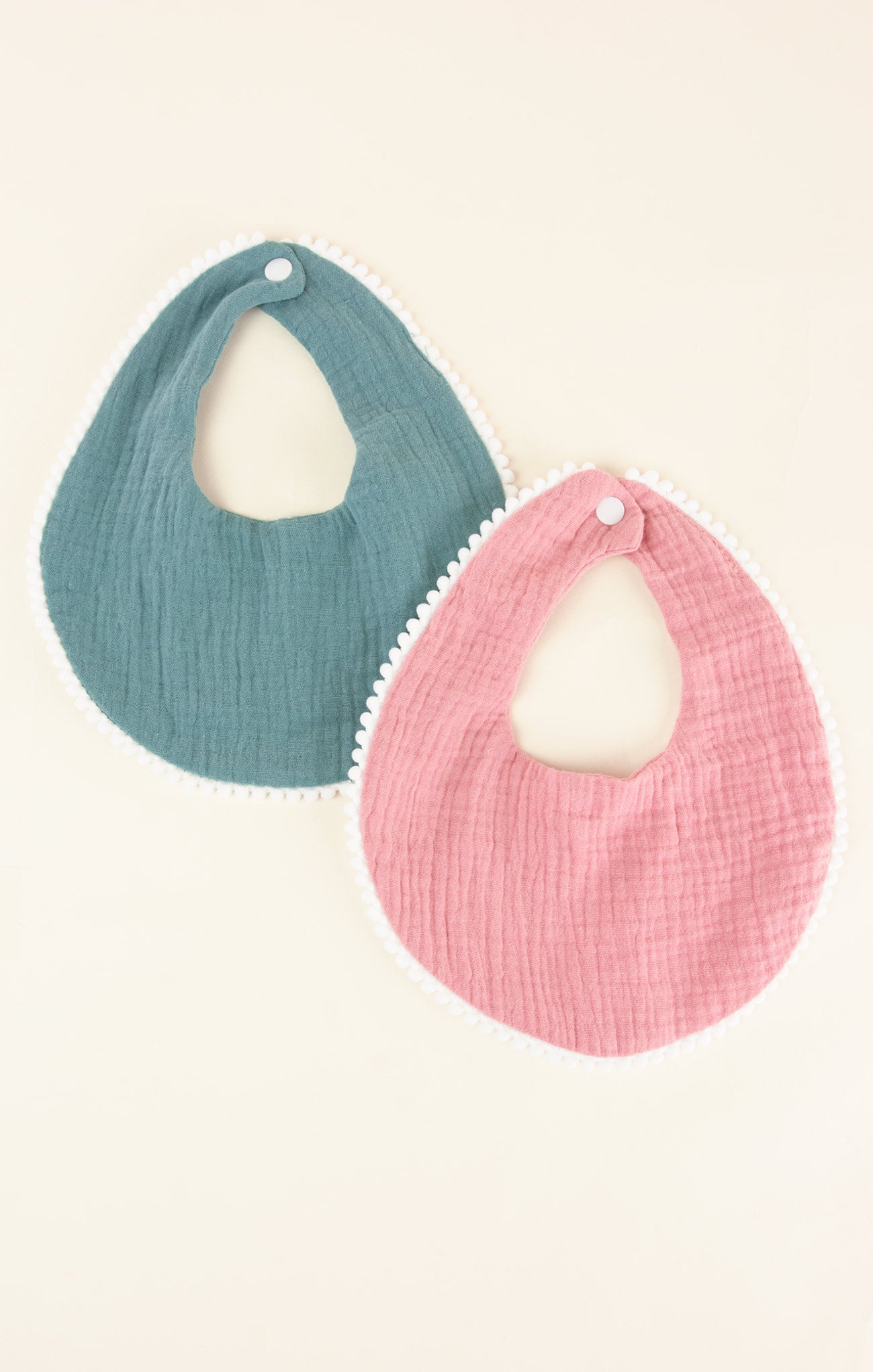 Two baby bibs, one blue and one pink, on a light beige background.