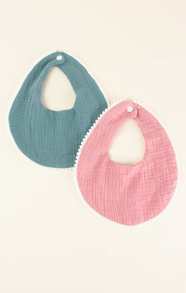 Two baby bibs, one blue and one pink, on a light beige background.
