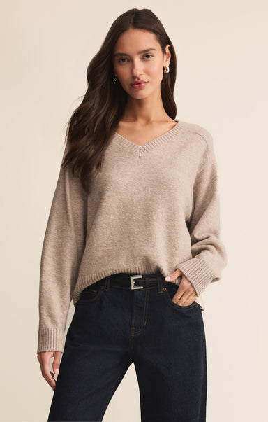 Woman wearing a beige sweater and dark jeans against a beige background