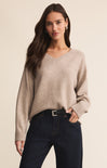 Woman wearing a beige sweater and dark jeans against a beige background