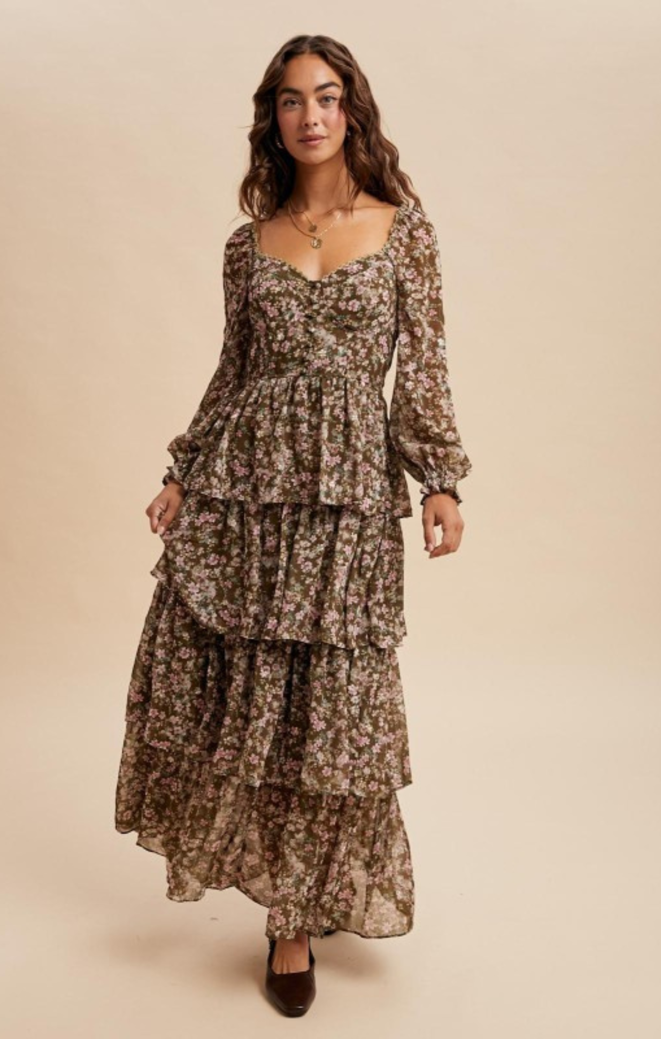 Woman wearing a long, tiered floral dress against a beige background