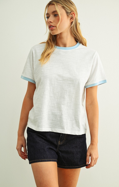 Woman wearing a white t-shirt with blue trim and black shorts on a plain background