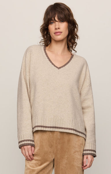 Woman wearing a beige sweater with brown trim against a plain background