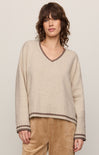 Woman wearing a beige sweater with brown trim against a plain background
