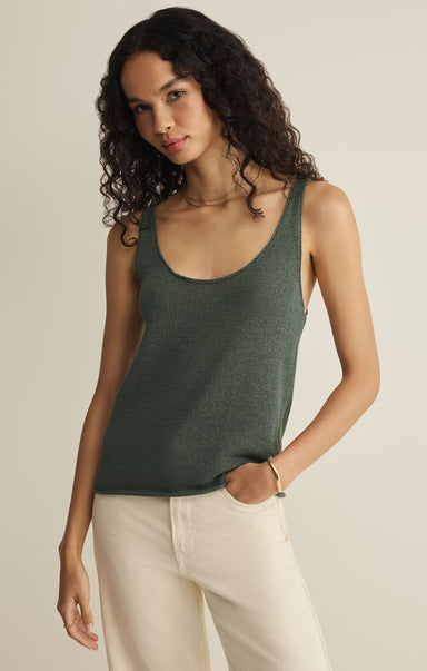 Woman wearing a green tank top and white pants against a plain background