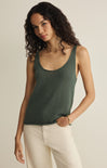 Woman wearing a green tank top and white pants against a plain background