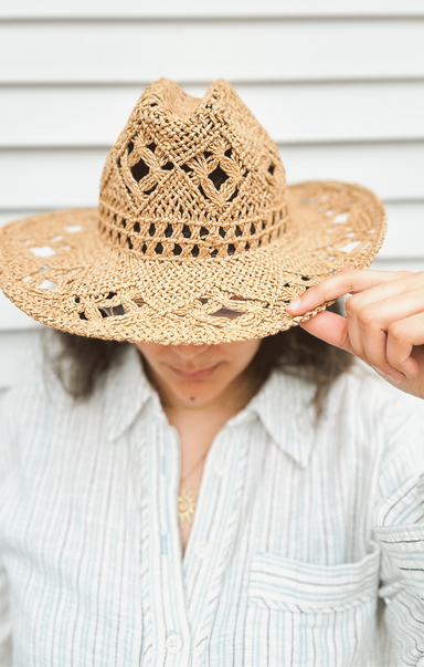 Person wearing a straw hat with intricate patterns against a neutral background