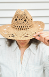 Person wearing a straw hat with intricate patterns against a neutral background
