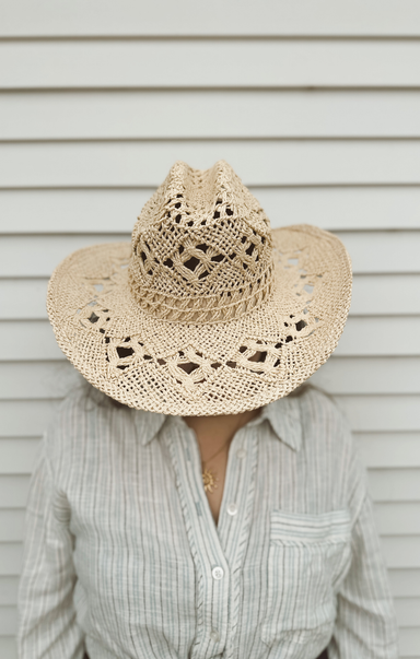 Person wearing a straw cowboy hat with a textured pattern against a neutral background